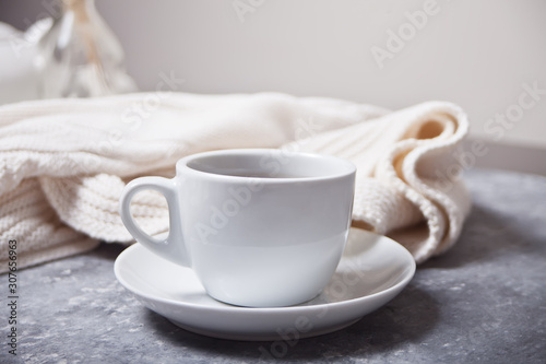 Close up of cup of coffee and knittead white plaid on the gray background