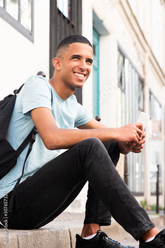 handsome young arabic man smiling outside with cellphone