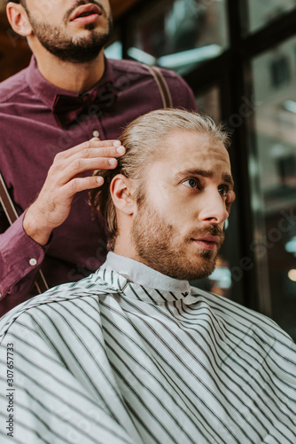 bearded barber touching hair of handsome man in barbershop