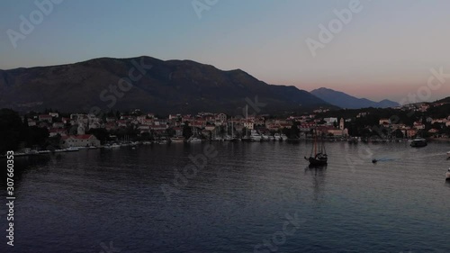 Aerial dolly shot of Cavtat harbor, Croatia. Calm water at sunset with a fishing boat navigating the moored boats.