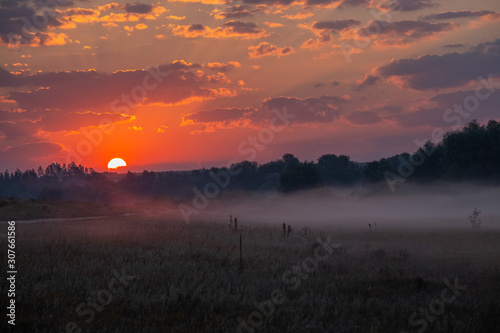 Sunrise through the clouds. Fog creeps across the meadow. © VASILEVS