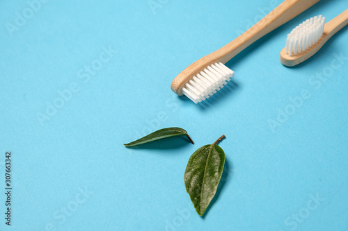Two wooden bamboo eco friendly toothbrushes and green leaf on blue background. Dental care and zero waste concept. Flat lay  top view  copy space