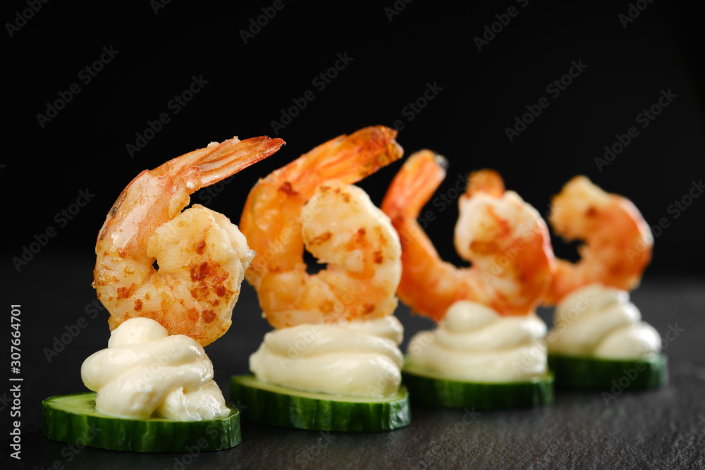 Delicious sauteed shrimp on cream cheese and sliced cucumber. black background closeup Delicious sauteed shrimp on cream cheese and sliced cucumber. black background closeup