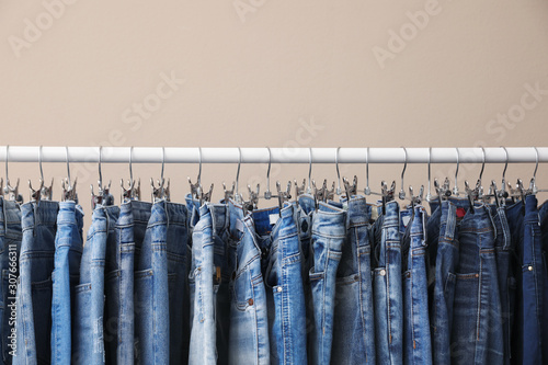 Rack with stylish jeans on beige background, closeup photo