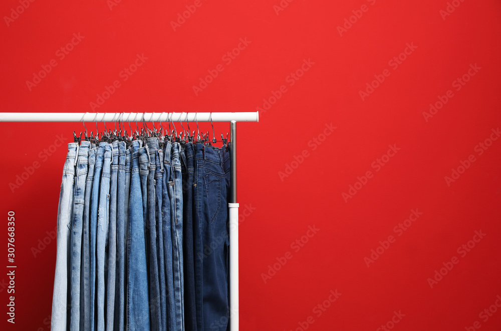 Rack with stylish jeans on red background. Space for text Rack with stylish jeans on red background. Space for text