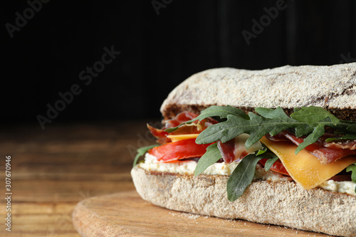 Delicious sandwich with fresh vegetables and prosciutto on wooden table, closeup. Space for text photo