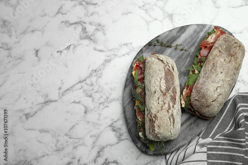 Delicious sandwiches with fresh vegetables and prosciutto on white marble table, top view. Space for text photo