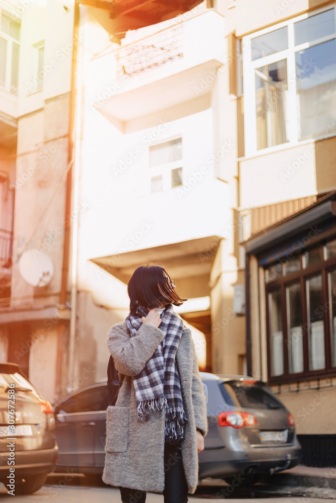 Attractive positive young girl wearing glasses in a coat on the background of buildings on cars Attractive positive young girl wearing glasses in a coat on the background of buildings on cars