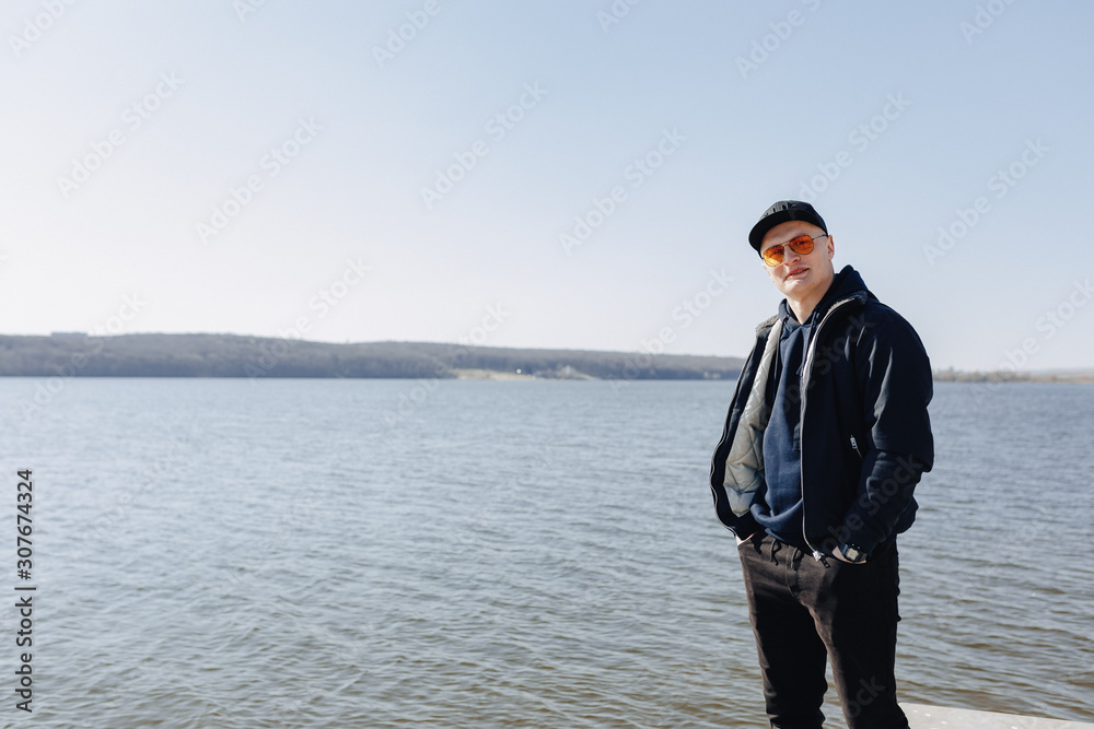 stylish young boy in orange glasses, jacket and cap, walk around the lake in spring or autumn