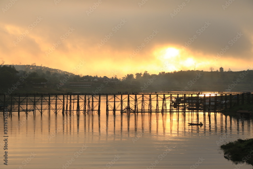 A little boat and wooden bridge with mountain landscape over the river at Sunrise in Thailand.