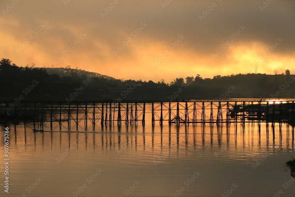 A wooden bridge with mountain landscape over the river at Sunrise in Thailand.