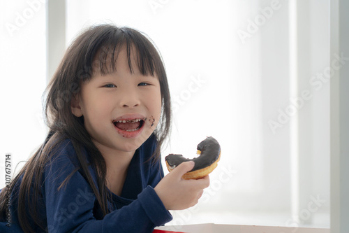 Close up face of hungry little Beautiful Asian girl eating chocolate donut, Cute kid eating donus with yummy face, Child eaitng snack photo