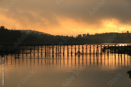 A wooden bridge with mountain landscape over the river at Sunrise in Thailand.