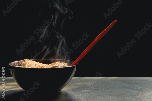 Steam and smoke Instant noodles in bowl on wooden table and nature light and black background, selective focus. It is a convenient and inexpensive food, but eating often is not good for health.