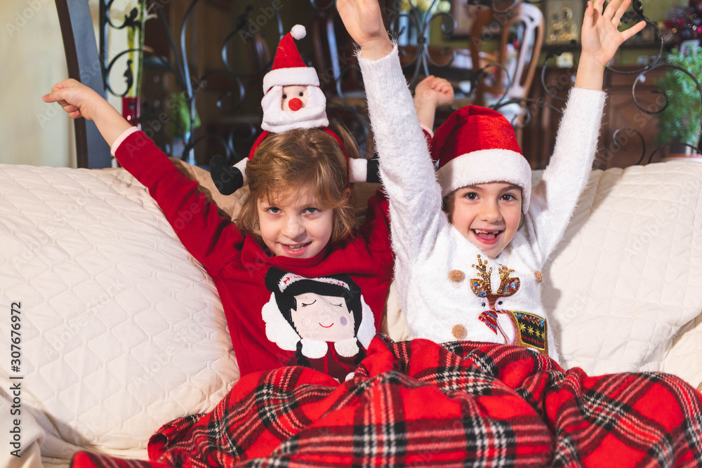 Obraz premium Girls sitting on the couch together, covered with blanket. Christmas time