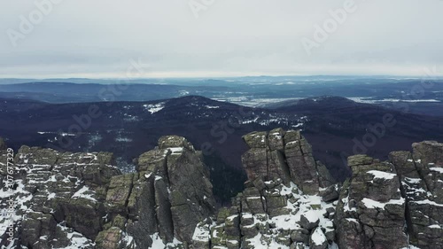 Aerial view; drone flies over rocky peaks of mountain ridge Otkliknoy Greben'; dangerous climbing route for tourists in winter; snow-covered stone and boulders; panorama of Ural mountains in foggy day photo