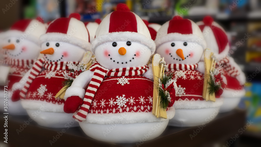 A toy snowman in a red sweater and hat holding wooden skis in his hands. New Year decorations, Christmas holiday toys. Greeting card with snowmen