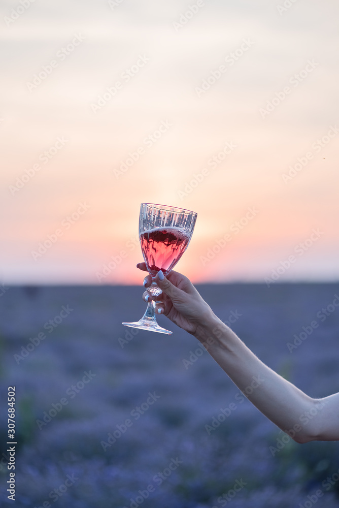 Girl with a glass of red wine in hands on a sunset lavender field