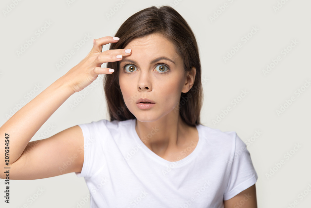 Headshot of surprised millennial woman notice first wrinkles on forehead Headshot of surprised millennial woman notice first wrinkles on forehead