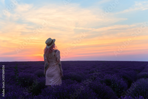 Beautiful slim girl in white dress and hat whirls in lavender field at sunset in summer