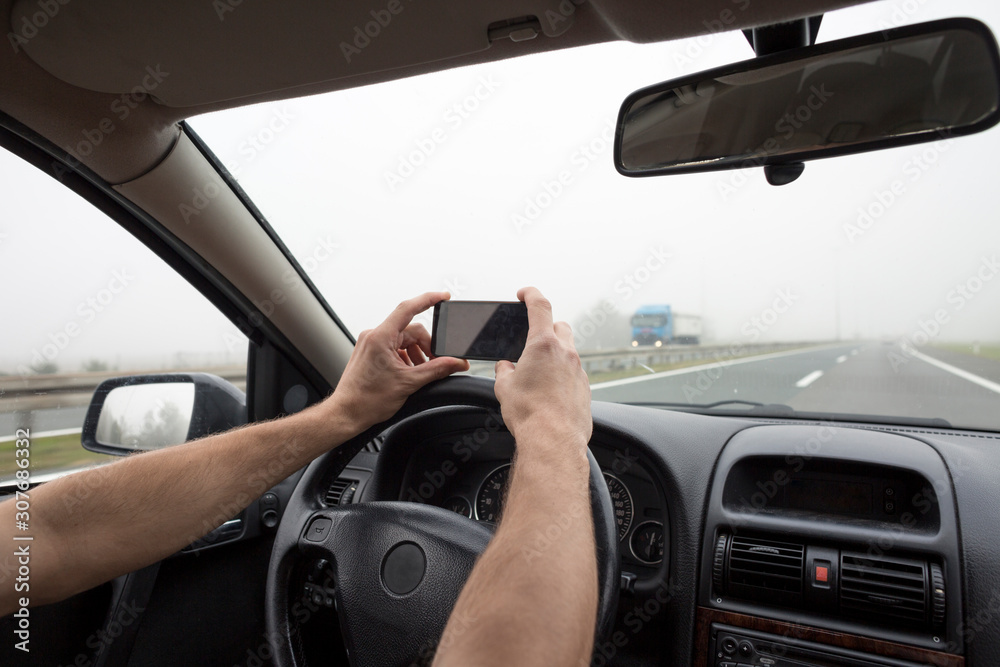 Use of smartphone in car. Man using phone while driving in fog on highway.