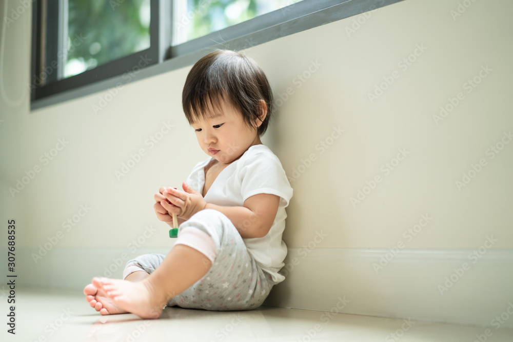 Asian cute baby sitting and playing a small toy sitting alone on floor at home. The kid holding the toy and question about how to play it. Play and learn of young child education concept Asian cute baby sitting and playing a small toy sitting alone on floor at home. The kid holding the toy and question about how to play it. Play and learn of young child education concept