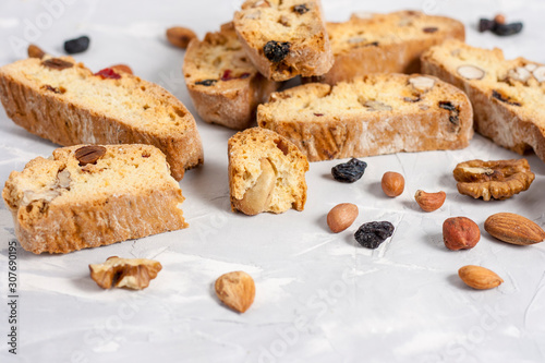 Tasty traditional Italian homemade biscotti or cantuccini cookies with hazelnuts  almonds  raisins and walnuts on a light gray background.