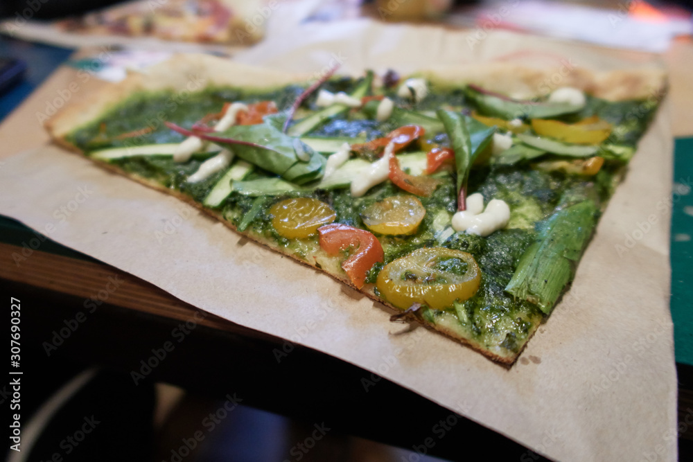 A fresh vegan organic vegetable pizza slice, with tomatoes, spinach, peppers, garlic, chilli, sliced spring onion and green pesto sauce. Street pizza new york and europe A fresh vegan organic vegetable pizza slice, with tomatoes, spinach, peppers, garlic, chilli, sliced spring onion and green pesto sauce. Street pizza new york and europe