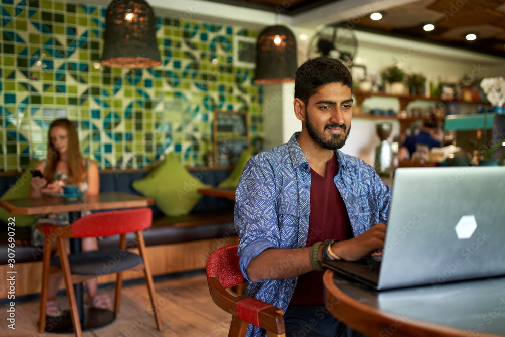 Handsome millennial indian man working in trendy coworking space