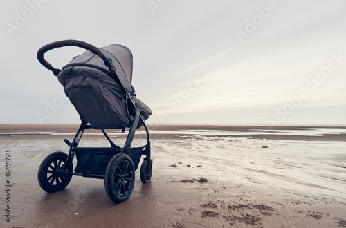 A infant baby childs stroller pushchair pram on a vast beach landscape at dusk and dawn. Relaxing and taking a holiday with children. Bonding travel with family in the great outdoors. photo