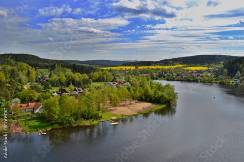 Beautiful village in woods along the river Vltava. Lush green trees, yellow fields, blue sky, white clouds. Roviště - Kamýk nad Vltavou, Czech Republic. 
