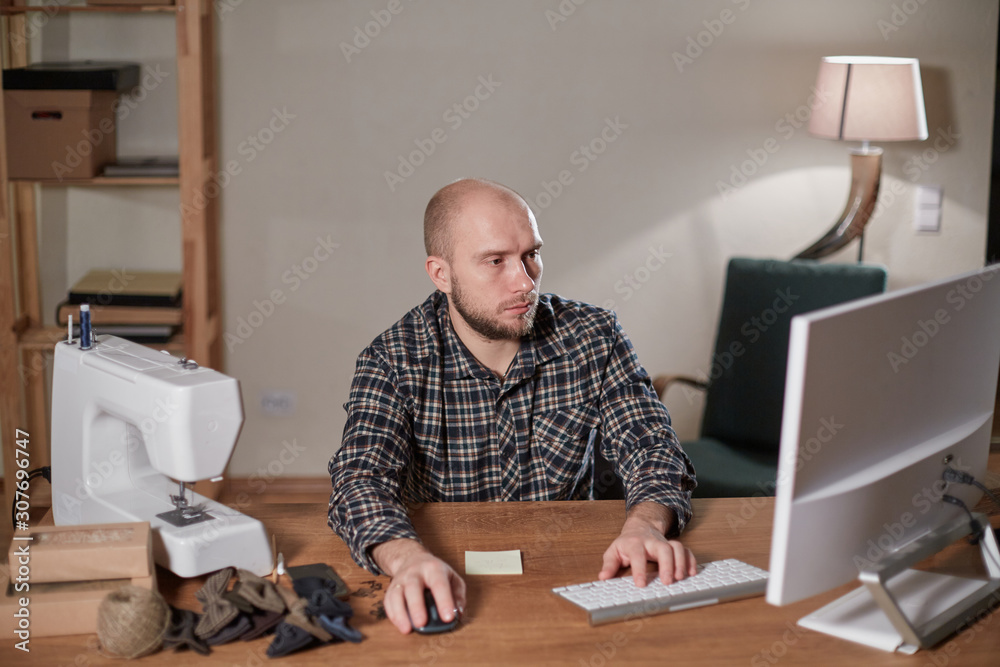 Man on the computer makes out the delivery of the online store. Working with sewing machine in a textile studio. Tailor makes bow ties of woolen fabric. Man on the computer makes out the delivery of the online store. Working with sewing machine in a textile studio. Tailor makes bow ties of woolen fabric.