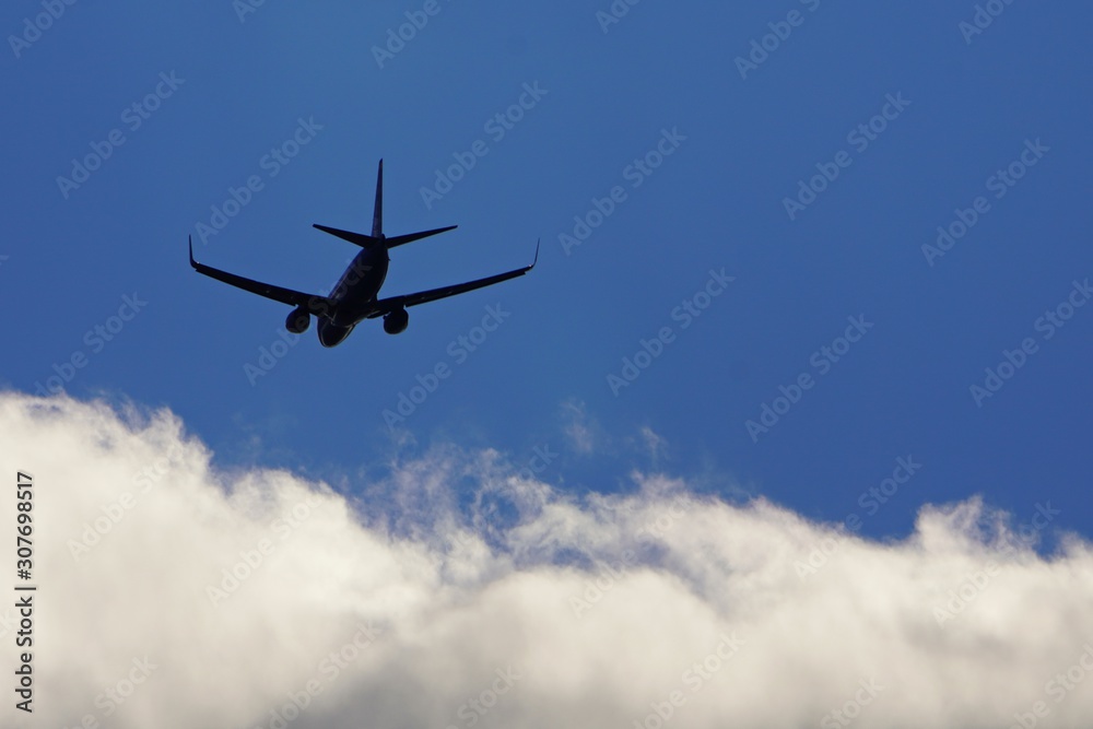 Silhouette of plane on blue sky flying towards white clouds Silhouette of plane on blue sky flying towards white clouds