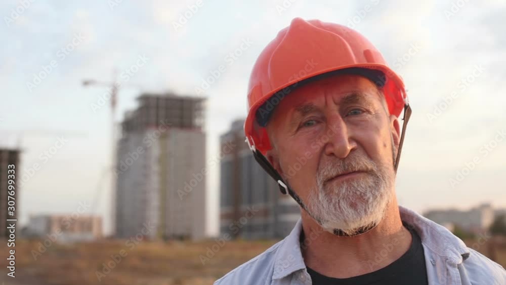 Builder engineer with a gray beard showing from hands symbol OK on the background of construction Builder engineer with a gray beard showing from hands symbol OK on the background of construction