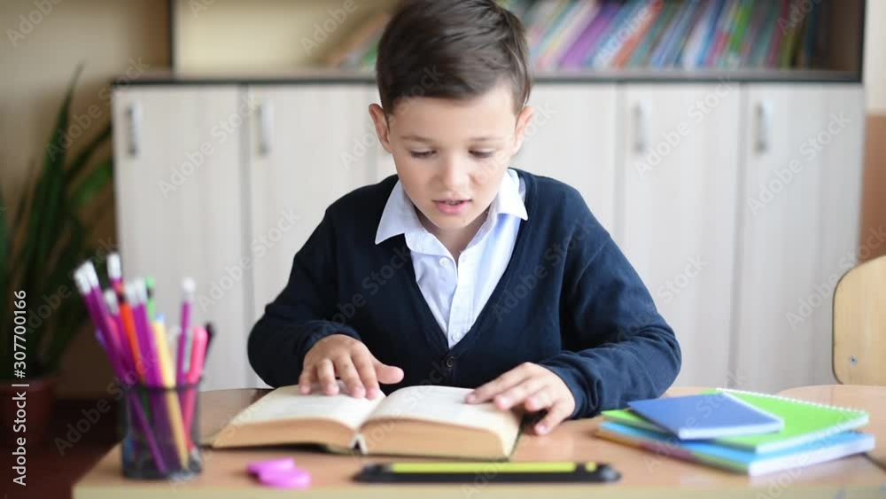 Funny schoolboy in uniform reading a textbook in classroom Funny schoolboy in uniform reading a textbook in classroom