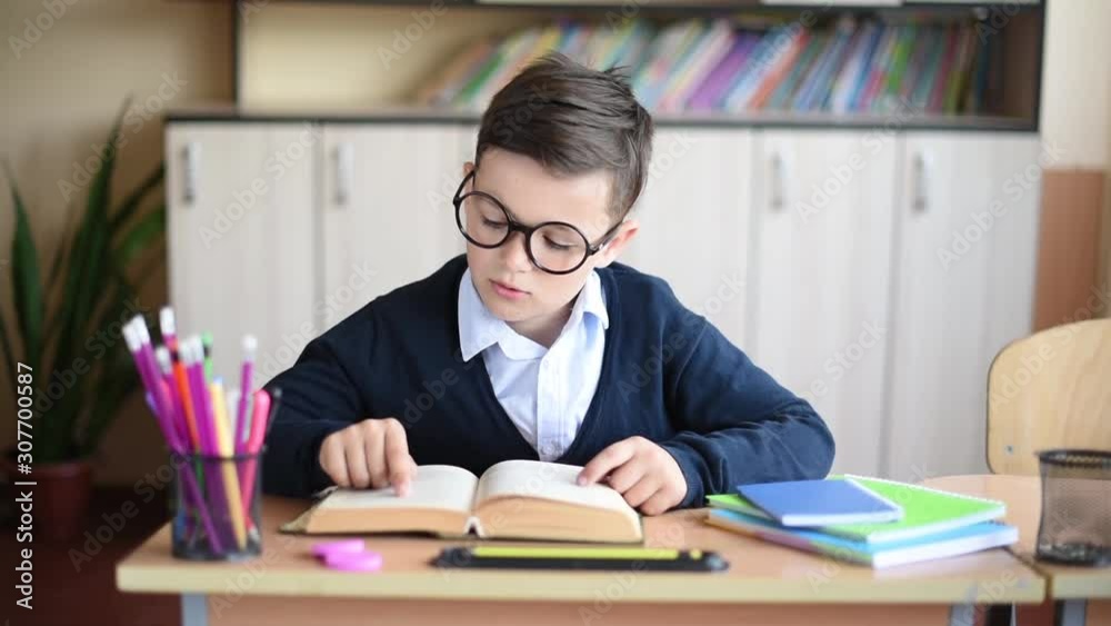 Funny schoolboy with glass in uniform reading a textbook in classroom Funny schoolboy with glass in uniform reading a textbook in classroom