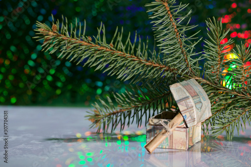 Open chest with gifts. A folded note is enclosed in it. Against the background of a fir branch and rainbow bokeh.