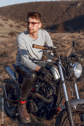 Handsome male in eyeglasses and gloves motorcyclist travels on motorbike, has adventure trip and feels extreme, likes active rest outside, drives and admiring place.