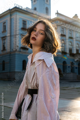 Waist up portrait of the stylish good looking young girl with wavy hair and red lips dressed in white striped shirt