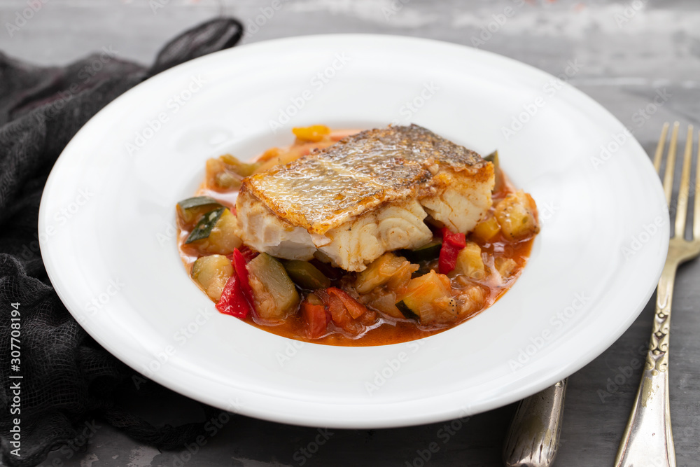 cod fish with vegetables in white plate on ceramic background