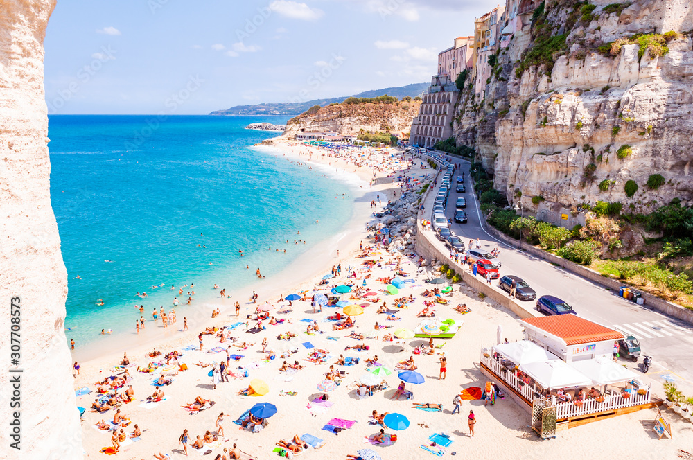Rotonda beach full of people. Amazing Italian beaches. Sea promenade scenery in Tropea with high cliffs with built on top city buildings and apartments.