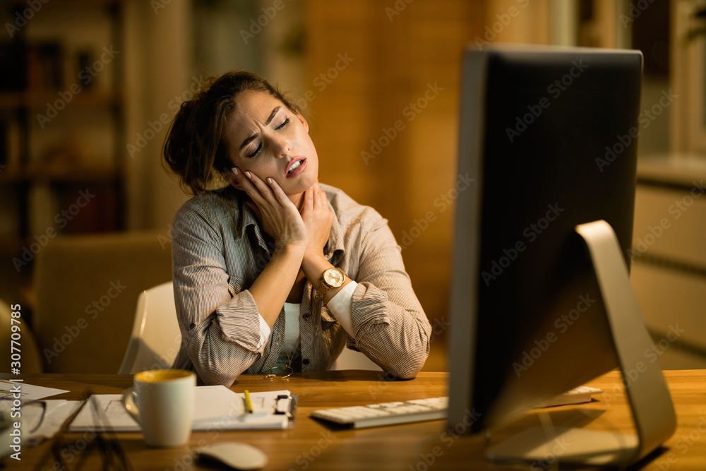 Young freelancer feeling pain in her neck while working late on a computer. Young freelancer feeling pain in her neck while working late on a computer.