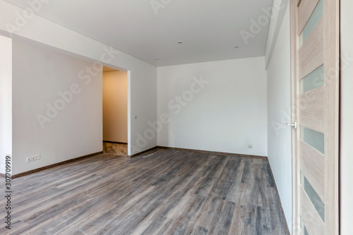 Empty room with white washed floating gray board laminate flooring. Newly painted white wall glass wooden doors and yellow corridor light in background for mockup
