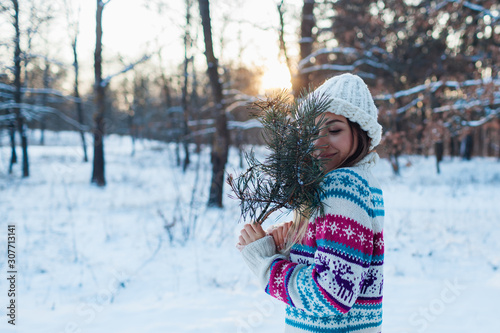 Winter walk. Young woman holding fir tree branches in forest enjoying snowy weather in knitted sweater