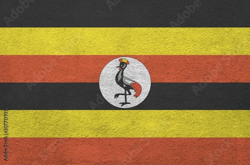 Uganda flag depicted in bright paint colors on old relief plastering wall. Textured banner on rough background photo