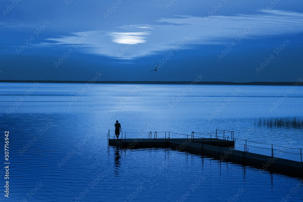 Man on pontoon pier in blue night. Color of the year 2020 Classic Blue pantone