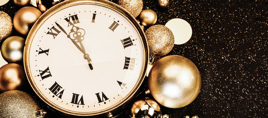 Gold vintage clock decorated with christmas balls on a black background in sparkles. Twelve o'clock, New Year 2020 is coming. Copy space