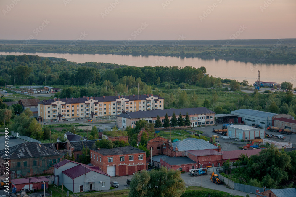 Small town with tiny houses near the river and green forests and fields. Trees and their shadows on the grass. Sundown and sunrises. View from high on the  landscape