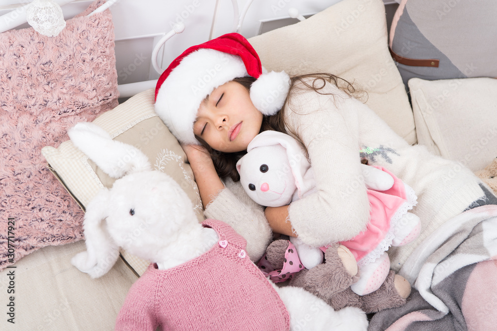 Fototapeta premium Magical morning. Christmas eve concept. Sweet home. Girl little kid relaxing on bed light interior with christmas decorations. Cozy room. Small child relaxing in bedroom. Kid lay in bed relaxing