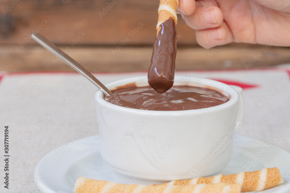 La mano de la persona sumerge los rollos de obleas en chocolate caliente
